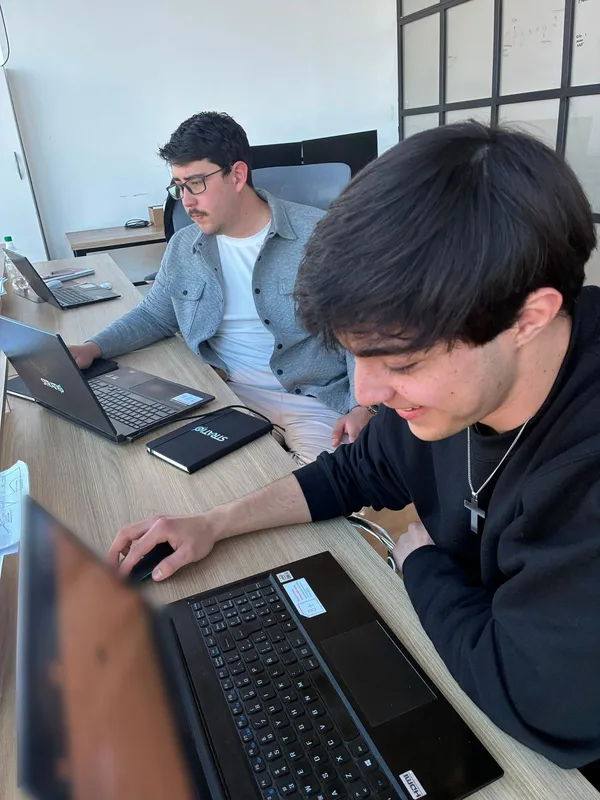 Dos personas del equipo trabajan en sus notebooks, sentadas a la misma mesa; sobre la mesa, un cuaderno de Stratio