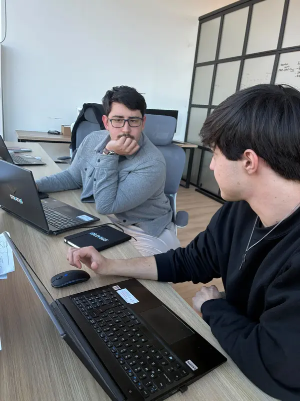 Dos personas del equipo trabajan en sus escritorios, cada una con su notebook